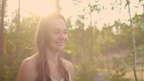 A-cute-girl-looks-into-the-camera-and-smiles-in-the-woods-in-the-sunny-sunset-rays